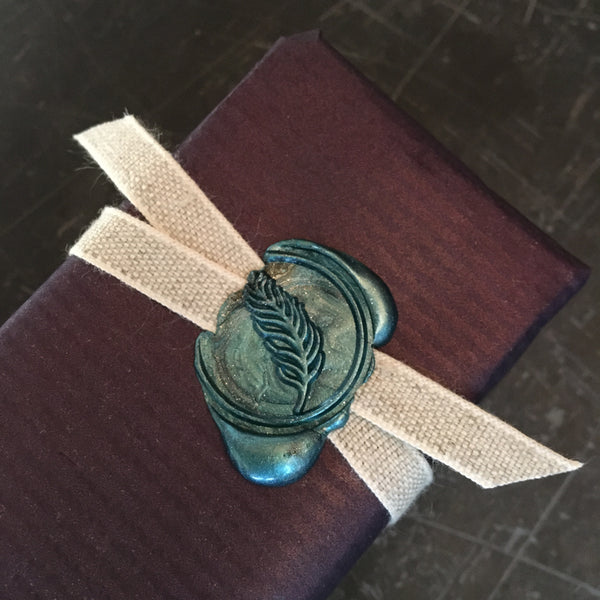 wrapped gift with a feather seal and beige ribbon on a dark surface