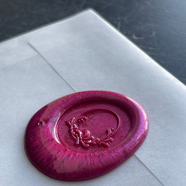 fushia  wax seal on a white envelope with wreath design 