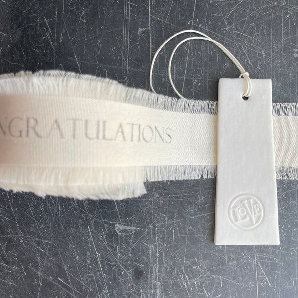 White ribbon with 'Congratulations' text and a white love tag on a scratched surface.