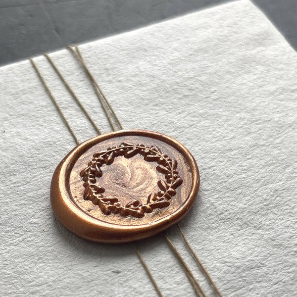 Bronze wax seal with laurel wreath design on a white envelope
