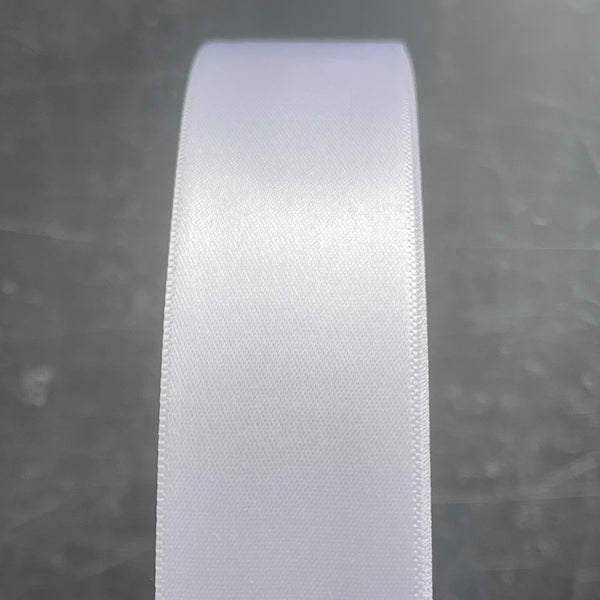 Close-up of a roll of white satin ribbon on a textured gray background