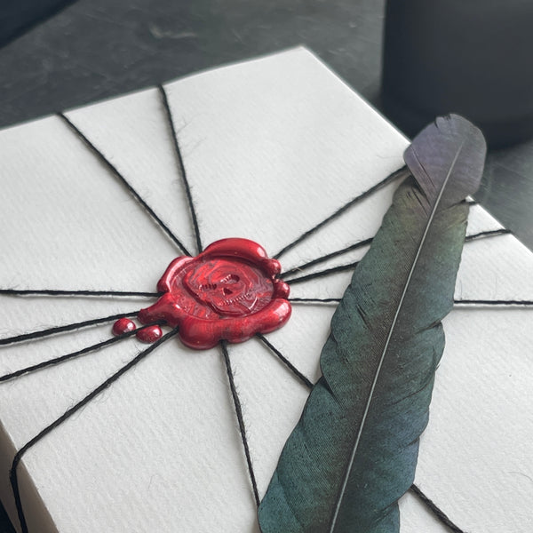 wax seal of a skull on white wrapping paper and a feather 