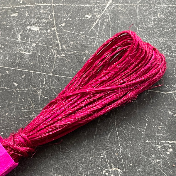 A selection of colorful fine hemp twine arranged in a row on a grey textured surface.