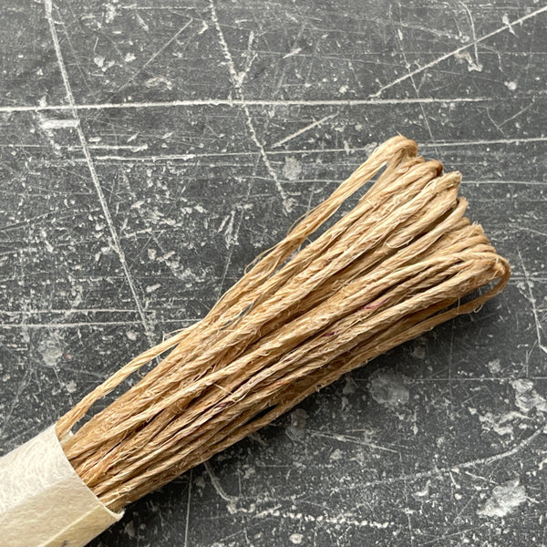 A selection of colorful fine hemp twine arranged in a row on a grey textured surface.