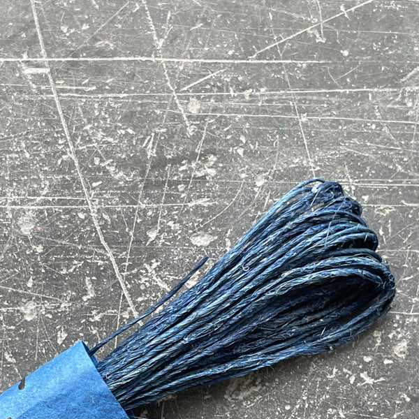 A selection of colorful fine hemp twine arranged in a row on a grey textured surface.