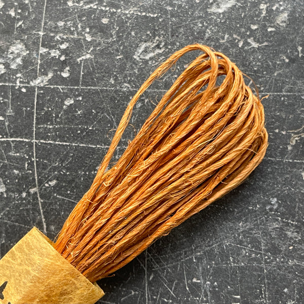 A selection of colorful fine hemp twine arranged in a row on a grey textured surface.